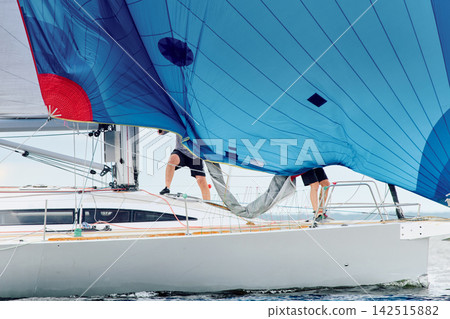 yachtsman assembles a light thin sail spinnaker during sailing regatta in the Gulf of Finland at sunny day, life jacket, board of the sailing boat, teamwork, reflections yachtsman assembles a light thin sail spinnaker during sailing regatta in the Gulf of Finland at sunny day, life jacket, board of the sailing boat, teamwork, reflections 142515882