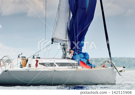 yachtsman assembles a light thin sail spinnaker during sailing regatta in the Gulf of Finland at sunny day, life jacket, board of the sailing boat, teamwork, reflections yachtsman assembles a light thin sail spinnaker during sailing regatta in the Gulf of Finland at sunny day, life jacket, board of the sailing boat, teamwork, reflections 142515906