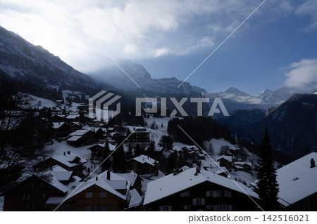 A beautiful winter scene in a Swiss Alps village, with snow-covered roofs and traditional mountain huts lining the streets. A beautiful winter scene in a Swiss Alps village, with snow-covered roofs and traditional mountain huts lining the streets. 142516021