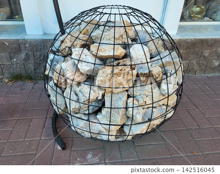 On a city street, there is a round gabion ball filled with colorful stones On a city street, there is a round gabion ball filled with colorful stones 142516045