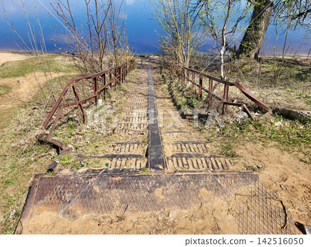 An old rusty iron staircase with railings leads down to the beach by the river. 142516050