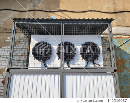 Outside, fans running on the wall in a box behind a grate Outside, fans running on the wall in a box behind a grate 142516087