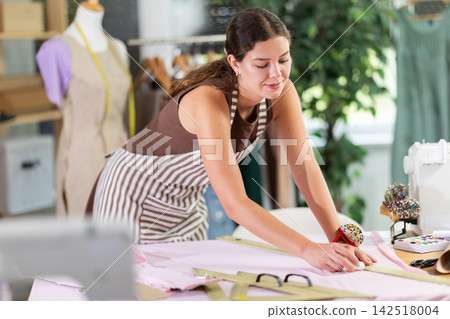 Female dressmaker making markings on fabric before cutting Female dressmaker making markings on fabric before cutting 142518004
