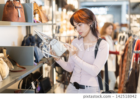Attentive young girl choosing handbag in clothing store Attentive young girl choosing handbag in clothing store 142518042