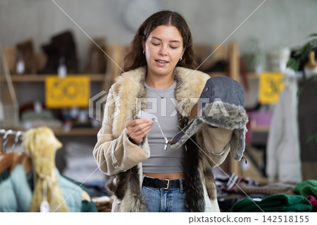 Young woman choosing fur hat in clothing store Young woman choosing fur hat in clothing store 142518155
