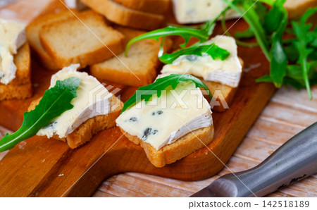On table there is cutting board with blue cheese and hardtack decorated with arugula 142518189