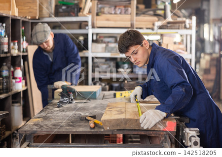 Young guy measuring wooden board with tape measure Young guy measuring wooden board with tape measure 142518205