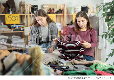 Latin woman customer examine and choose sweater in store Latin woman customer examine and choose sweater in store 142518223