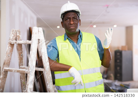 Portrait of disgruntled african american worker in yellow vest in cottage under construction Portrait of disgruntled african american worker in yellow vest in cottage under construction 142518330
