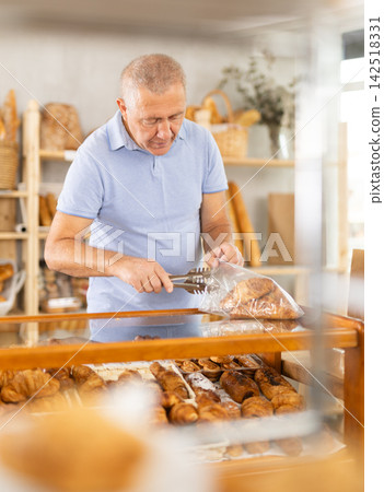 Elderly man buyer puts croissants in bag Elderly man buyer puts croissants in bag 142518331