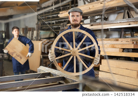 Portrait of an experienced carpenter holding wooden cart wheel in his hands Portrait of an experienced carpenter holding wooden cart wheel in his hands 142518334