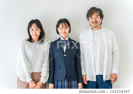 一位身穿校服的高中女生站在笑容滿面的父母身旁。一家三口即將迎來新學期或畢業典禮。 142518347