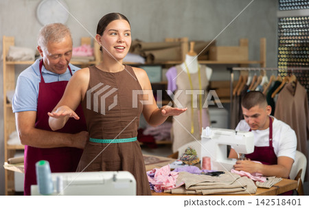 Elderly tailor taking measurements from woman next to worker Elderly tailor taking measurements from woman next to worker 142518401