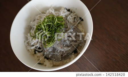 A two-color rice bowl with fresh raw and boiled whitebait, topped with shiso leaves. A two-color rice bowl with fresh raw and boiled whitebait, topped with shiso leaves. 142518420