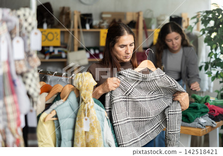 During November sales, Latin woman choose coat, other client in background During November sales, Latin woman choose coat, other client in background 142518421
