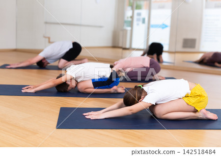Tween children performing resting asana Balasana with parents in gym Tween children performing resting asana Balasana with parents in gym 142518484