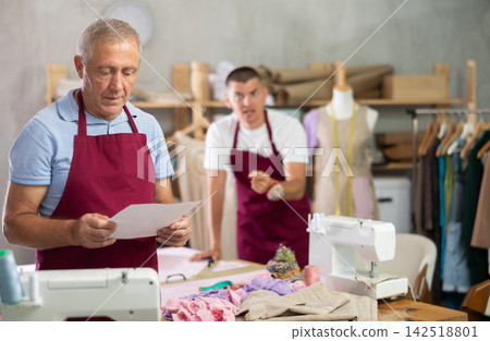 Young guy tailor scolding assistant with document for dismissal Young guy tailor scolding assistant with document for dismissal 142518801
