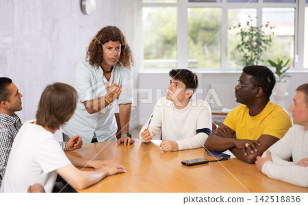 Middle-aged man instructor explaining the topic to group of guys around the table Middle-aged man instructor explaining the topic to group of guys around the table 142518836