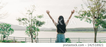 Freedom happy girl feeling alive and free in nature breathing clean and fresh air, enjoying bright summer day near lake with raised arms and positive energy during outdoor leisure trip Freedom happy girl feeling alive and free in nature breathing clean and fresh air, enjoying bright summer day near lake with raised arms and positive energy during outdoor leisure trip 142518921
