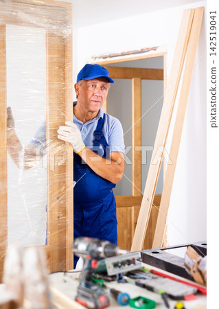 Portrait of professional door installer with new door in room being renovated Portrait of professional door installer with new door in room being renovated 142519041