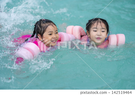 two preschool child girl playing and swimming with floaties in pool water two preschool child girl playing and swimming with floaties in pool water 142519464
