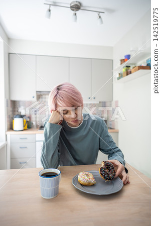 Mature woman looks stressed beside donuts while resisting PMS cravings and sugar addiction. Mature woman looks stressed beside donuts while resisting PMS cravings and sugar addiction. 142519775