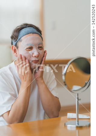 一位四十多歲的男子在鏡子前仔細地將面膜敷在臉上,展示他的男士美容護膚流程。 一位四十多歲的男子在鏡子前仔細地將面膜敷在臉上,展示他的男士美容護膚流程。 142520243
