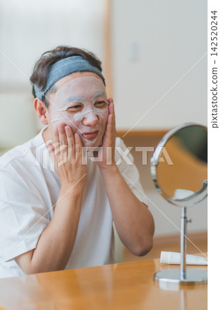 A 40-something man smiling in front of the mirror while wearing a sheet mask - Men's Beauty A 40-something man smiling in front of the mirror while wearing a sheet mask - Men's Beauty 142520244