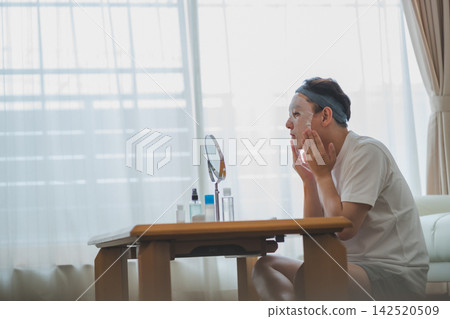 A 40-year-old man checks his cheeks in the mirror while wearing a sheet mask - Men's Beauty A 40-year-old man checks his cheeks in the mirror while wearing a sheet mask - Men's Beauty 142520509