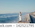 A woman with a camera stands on the breakwater, gazing at the sea. 142521795
