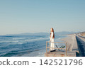 A woman with a camera stands on the breakwater, gazing at the sea. 142521796