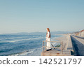 A woman with a camera stands on the breakwater, gazing at the sea. 142521797