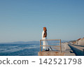 A woman with a camera stands on the breakwater, gazing at the sea. 142521798