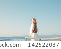 A young woman looks back from a breakwater with the blue sky and sea as a backdrop. 142522037