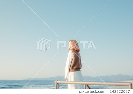 A young woman looks back from a breakwater with the blue sky and sea as a backdrop. A young woman looks back from a breakwater with the blue sky and sea as a backdrop. 142522037
