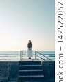 A young woman with her back to the camera, gazing at the blue sky and the sea. 142522052