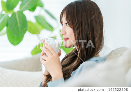 一位女士一邊喝牛奶一邊放鬆。這是一段專注於美麗和健康的舒適時光。 一位女士一邊喝牛奶一邊放鬆。這是一段專注於美麗和健康的舒適時光。 142522298