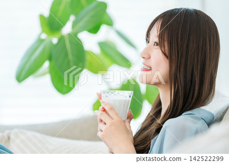 一位女士一邊喝牛奶一邊放鬆。這是一段專注於美麗和健康的舒適時光。 一位女士一邊喝牛奶一邊放鬆。這是一段專注於美麗和健康的舒適時光。 142522299