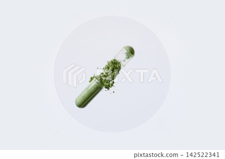 Open transparent capsule spilling green powder on white surface Open transparent capsule spilling green powder on white surface 142522341