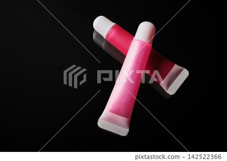 Shiny pink and red lip gloss tubes displaying cosmetic beauty products Shiny pink and red lip gloss tubes displaying cosmetic beauty products 142522366