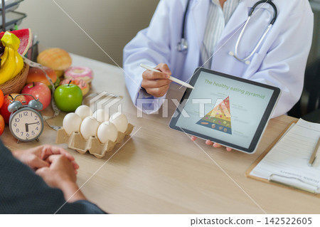 Nutritionist presenting healthy eating pyramid on tablet to patient in clinic consultation Nutritionist presenting healthy eating pyramid on tablet to patient in clinic consultation 142522605