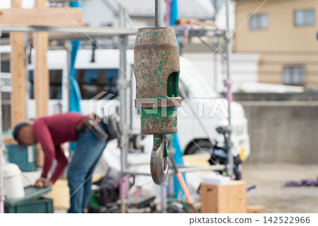 A crane hook used at a residential construction site. The workers and the construction of the house. A crane hook used at a residential construction site. The workers and the construction of the house. 142522966