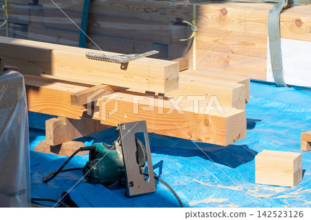 Lumber and circular saws lined up at a wooden house construction site. Building materials and tools that support the work of carpenters. Lumber and circular saws lined up at a wooden house construction site. Building materials and tools that support the work of carpenters. 142523126