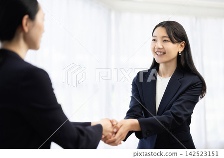 A young Japanese businesswoman in a suit smiles and shakes hands with a customer. A young Japanese businesswoman in a suit smiles and shakes hands with a customer. 142523151