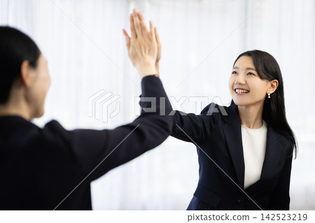 一位身穿職業套裝的年輕日本女商人面帶微笑，與一位顧客擊掌。 142523219