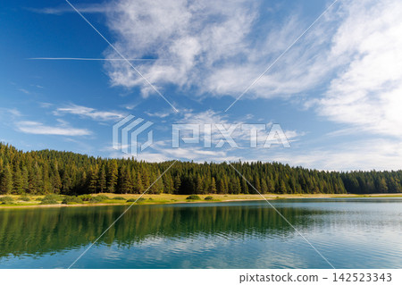 Calm lake with forest reflection under blue sky Calm lake with forest reflection under blue sky 142523343