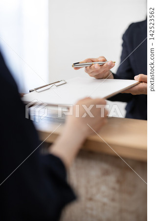 A close-up of the hands of a woman in a suit handing over documents and a pen. A close-up of the hands of a woman in a suit handing over documents and a pen. 142523562