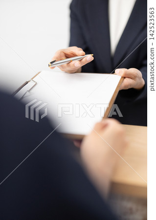 A close-up of the hands of a woman in a suit handing over documents and a pen. A close-up of the hands of a woman in a suit handing over documents and a pen. 142523563