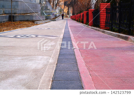 Close-up street strip of pedestrian sidewalk from lower angle, separating lanes intended for movement of passers-by on left side for the passage of cyclists, mopeds, scooters, on right, painted red Close-up street strip of pedestrian sidewalk from lower angle, separating lanes intended for movement of passers-by on left side for the passage of cyclists, mopeds, scooters, on right, painted red 142523799