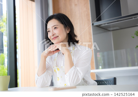 一位中年婦女的特寫鏡頭，她可能是 50 多歲的家庭主婦，穿著圍裙，在自家廚房微笑。 142525164